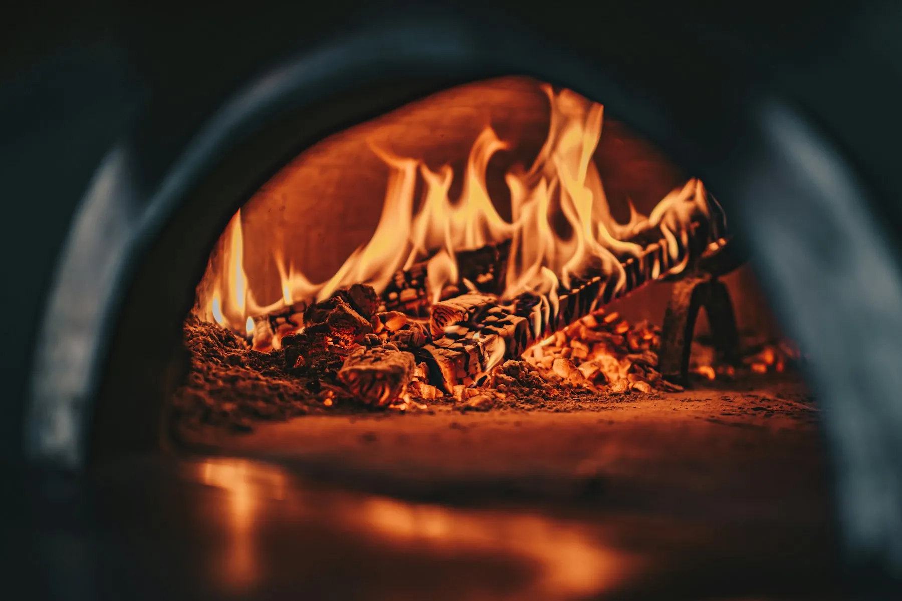 Flames roaring over oak logs inside a black wood-fired oven