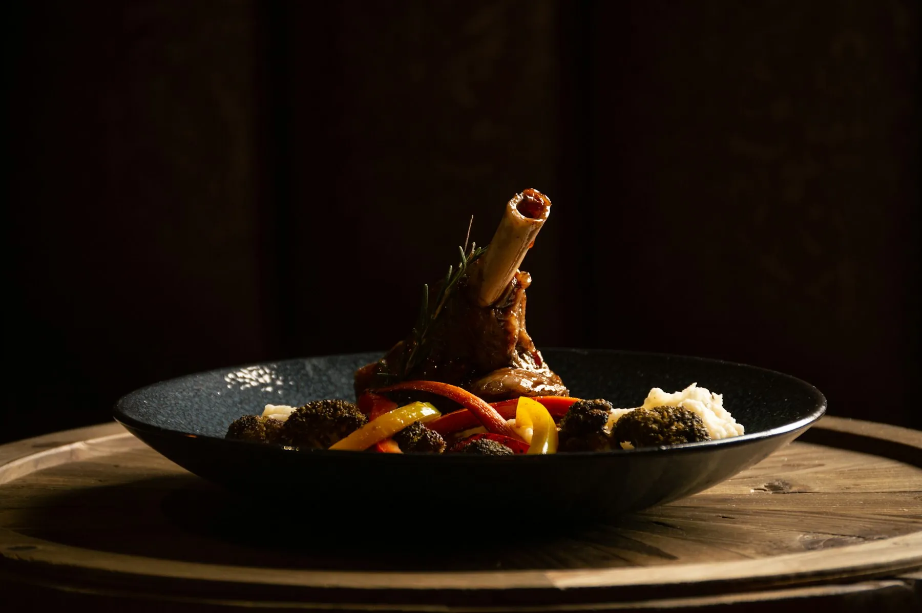 A braised lamb shank with roasted peppers in a dark bowl