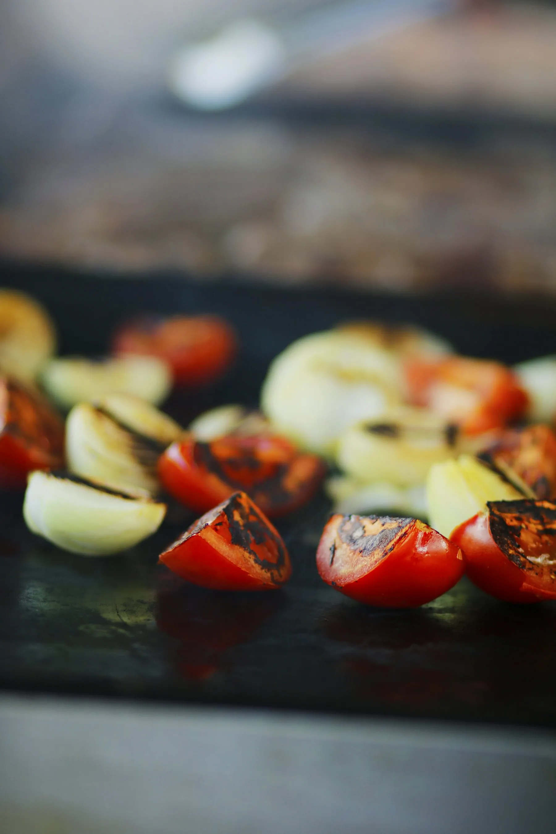Charred tomatoes and onion wedges on a dark grill